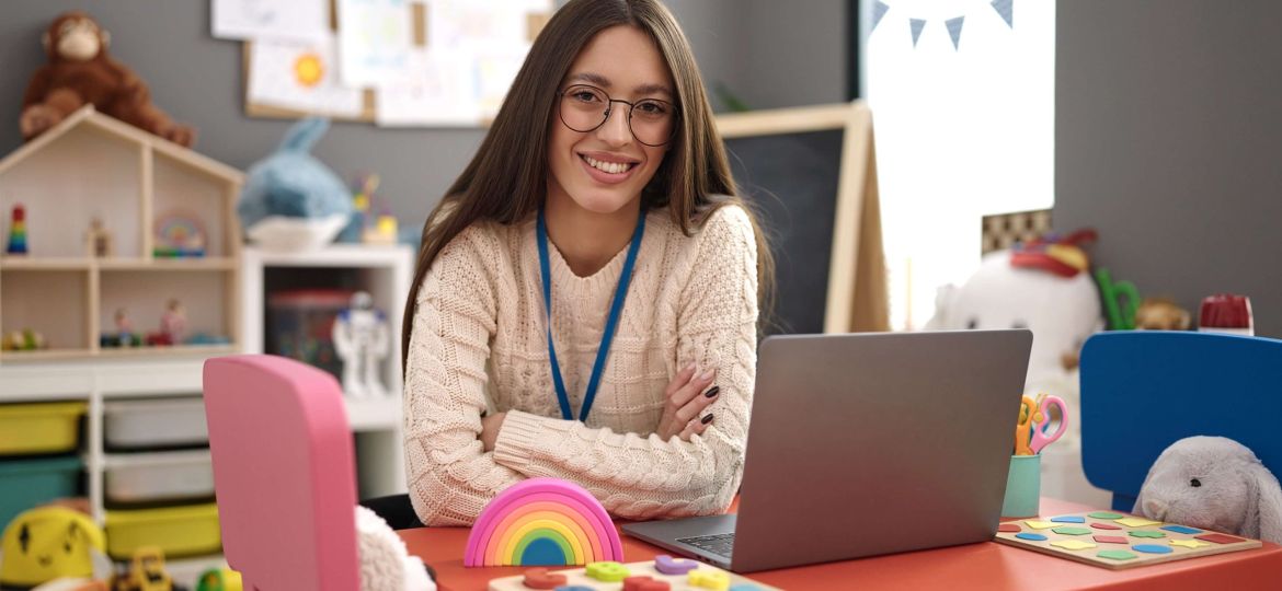 dziewczyna siedzi przy biurku z laptopem w pokoju dziecięcym pełnym edukacyjnych zabawek